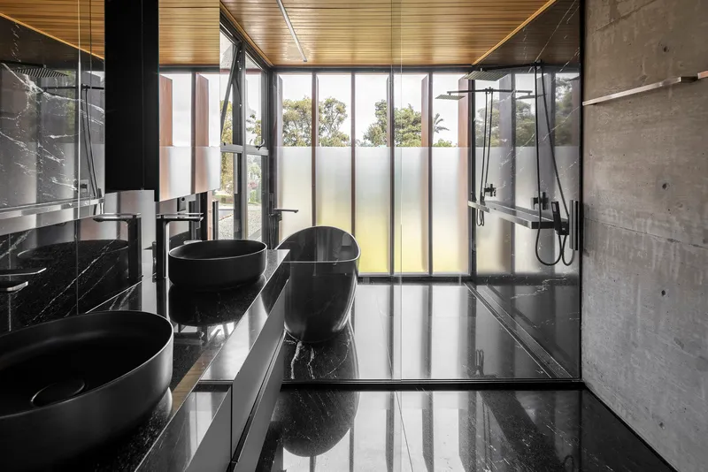 Bathroom with black marble surfaces, concrete walls, and translucent glazing panels with daylight