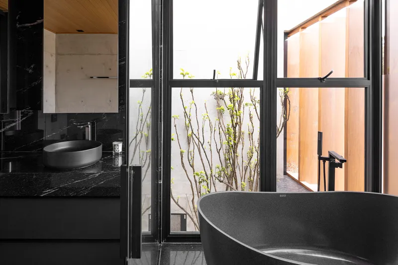 Freestanding bathtub beside steel-framed window with planted courtyard beyond