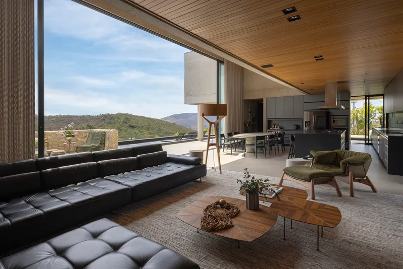 Open-plan living space with timber ceiling and full-height glazing overlooking forested hills