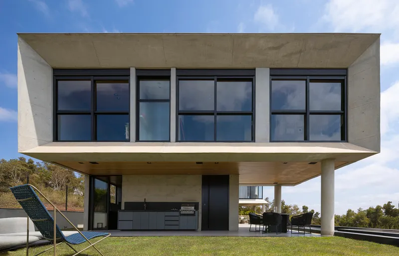 Cantilevered concrete upper volume with grid windows above a covered outdoor kitchen