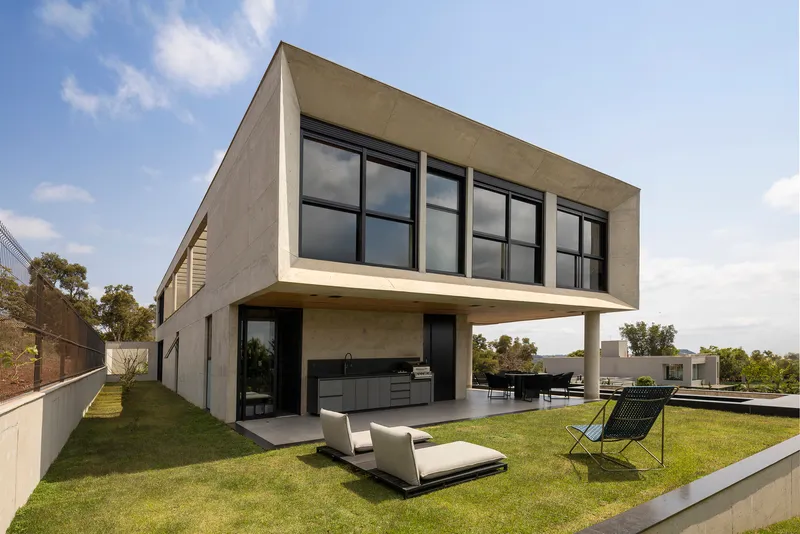 Elevated concrete box supported by cylindrical columns above lawn and outdoor loungers
