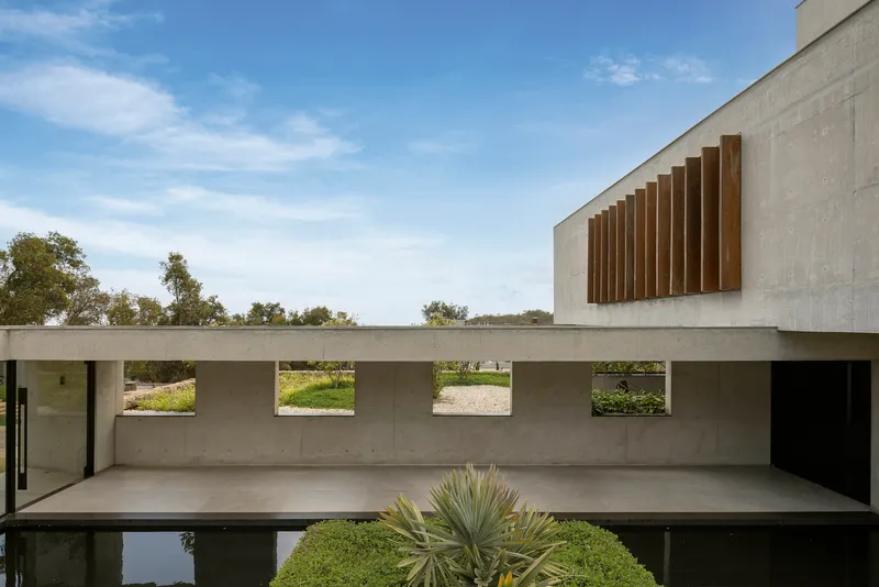 Concrete terrace with horizontal slot windows reflected in a still pool edged by agave plants