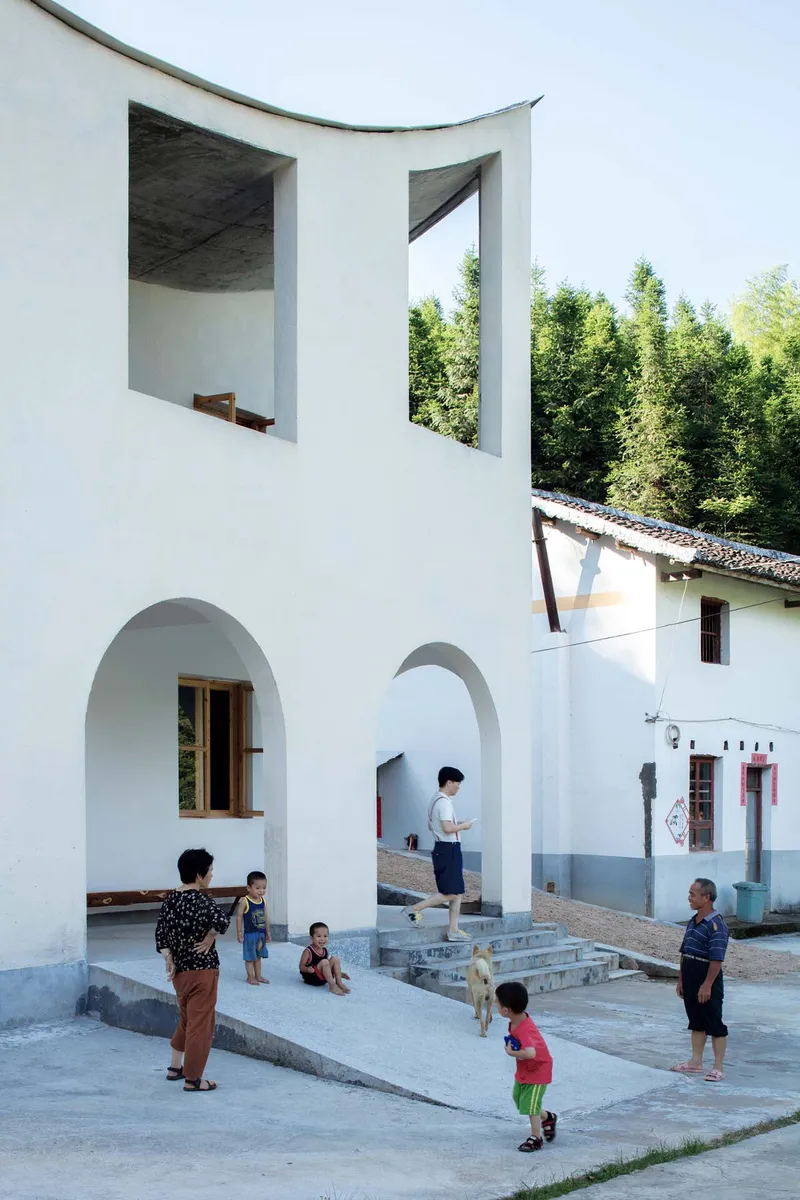 White courtyard with arched openings and children playing on stone pavement beneath curved concrete ceiling openings