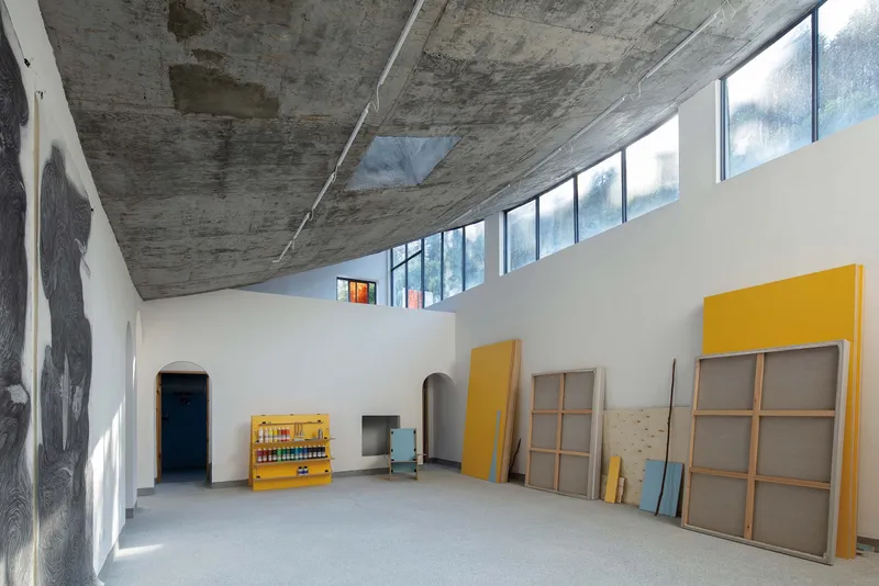 Interior hall with exposed board-formed concrete ceiling and clerestory windows above white walls and stored yellow panels