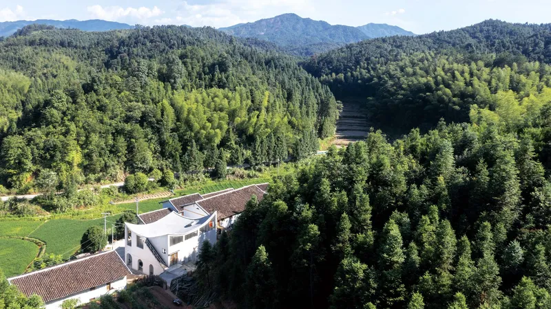 Aerial view of white compound with undulating roof set among forested hills and cultivated fields