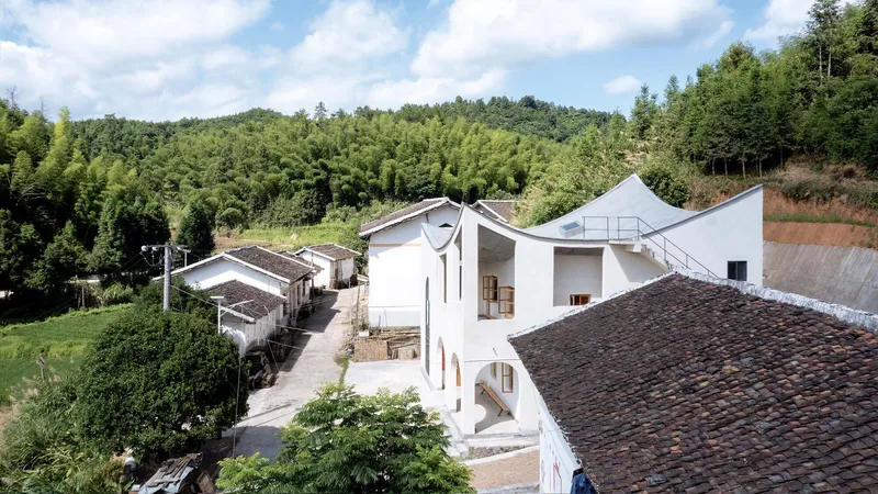 Elevated view showing white volumes with flowing roof forms rising above existing tile roofed structures