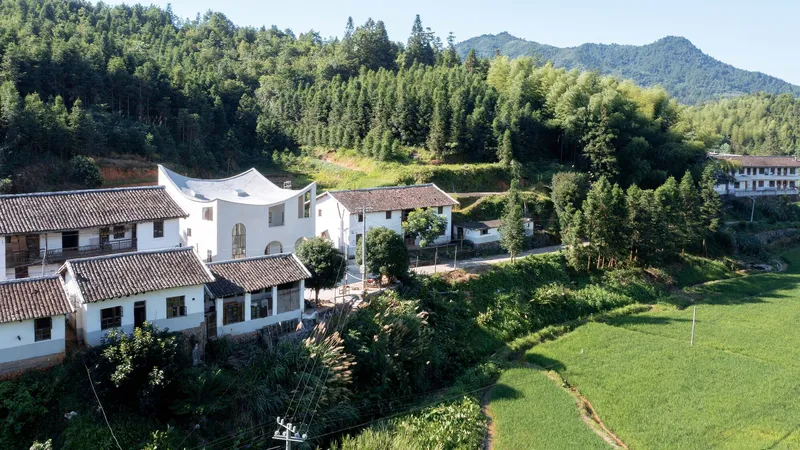 Aerial view of white-walled courtyard houses with tiled roofs nestled among forested hills and terraced farmland