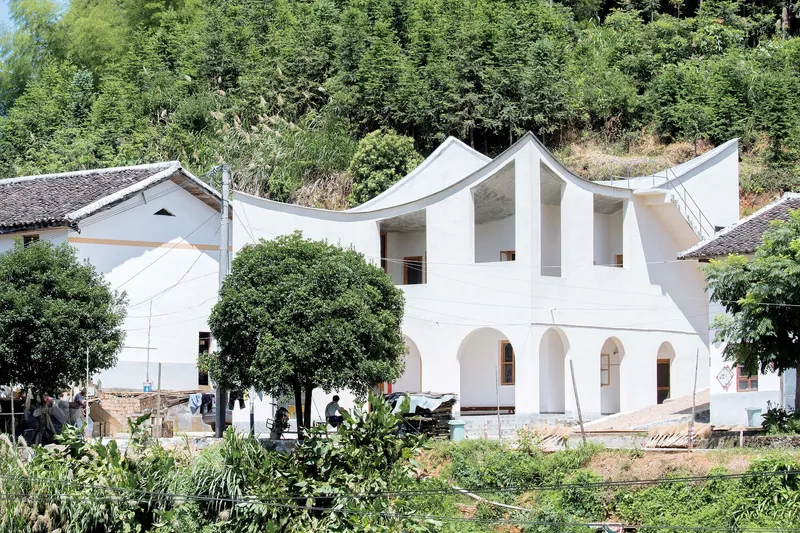 White facade with arched openings and three undulating roof peaks framed by lush vegetation and neighboring houses