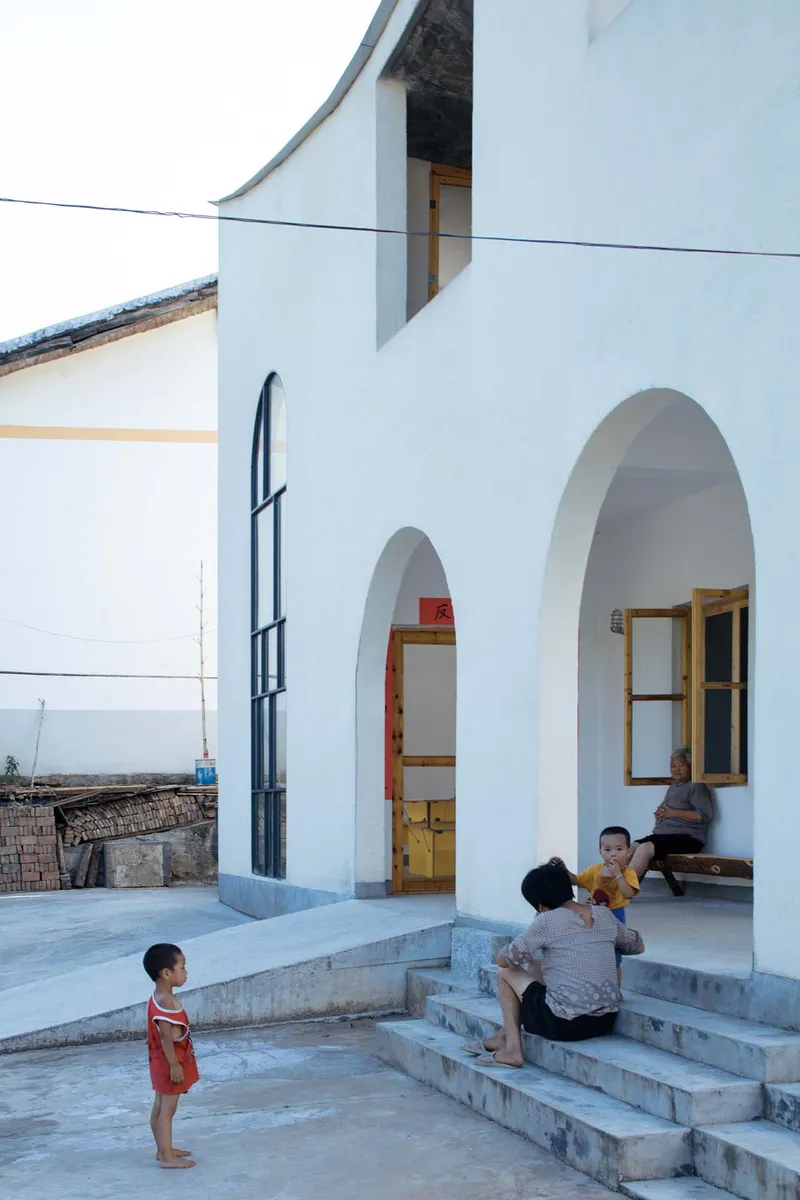 Stone steps leading to arched doorways where two children and an adult sit in the shade