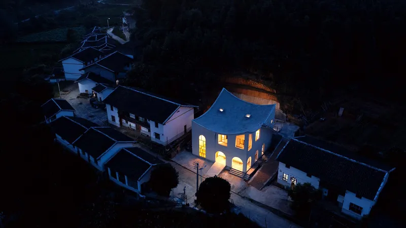 Aerial view at dusk showing the illuminated arched windows against the dark surrounding village rooftops