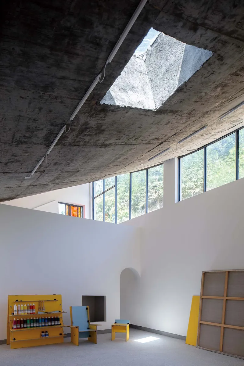 Angular skylight opening in the raw concrete ceiling above white gallery walls with yellow furniture