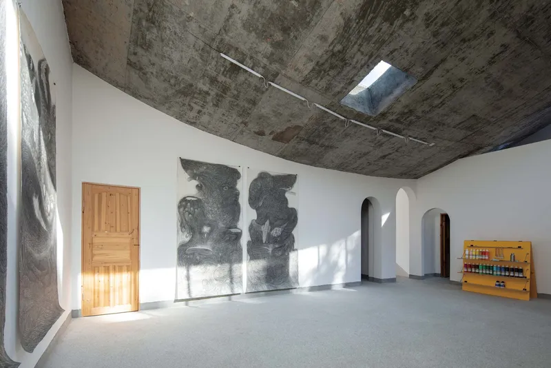 White-walled gallery corner with arched doorways, timber door, and textured concrete ceiling with skylight