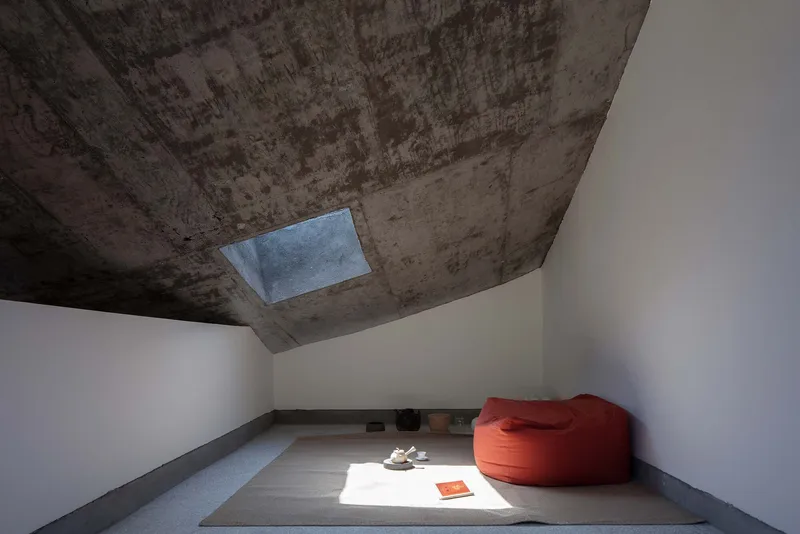 Minimalist room with board-formed concrete ceiling, rectangular skylight, raised platform, and orange bean bag