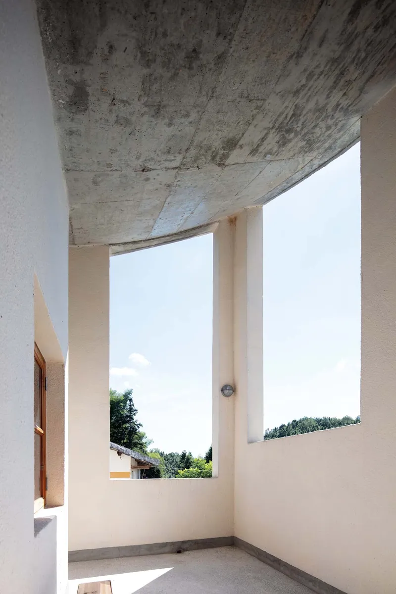 Corner terrace with exposed concrete ceiling soffit and tall window openings framing distant trees