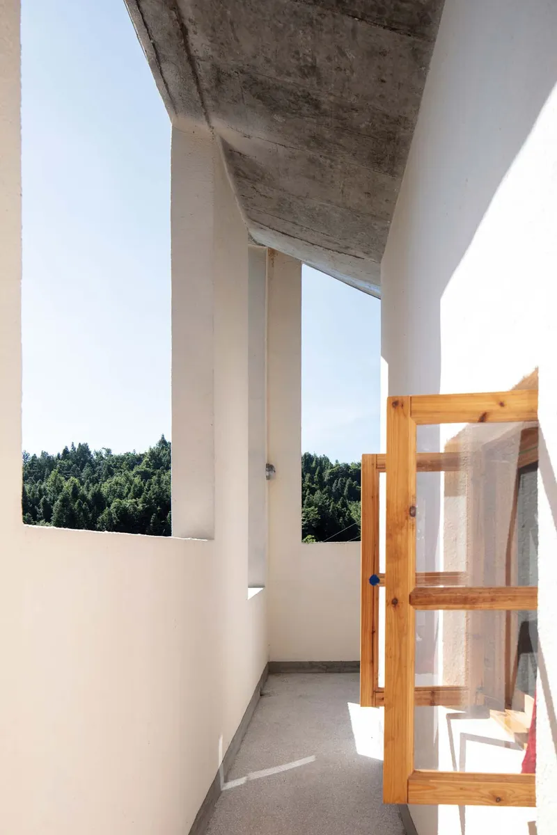 Narrow balcony with board-formed concrete soffit and timber window frame overlooking forested hills