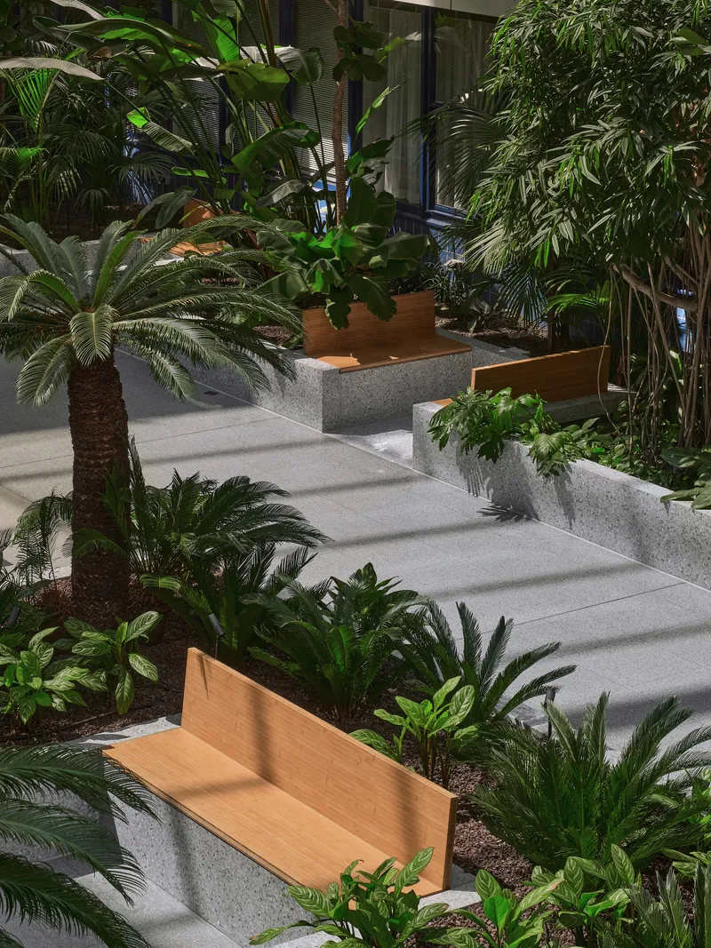 Terraced concrete planters with timber benches and tropical vegetation beneath an interior atrium skylight