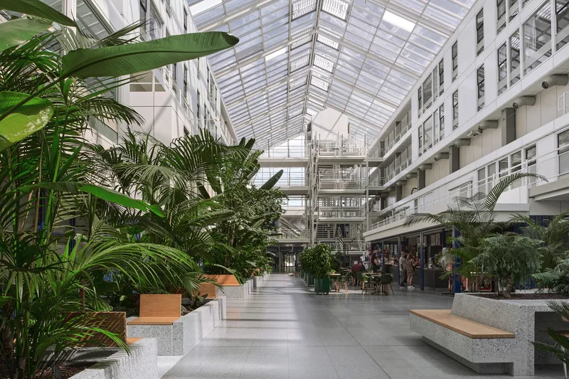 Interior atrium with glazed skylight, planted beds with palms, and terrazzo benches along polished concrete floor