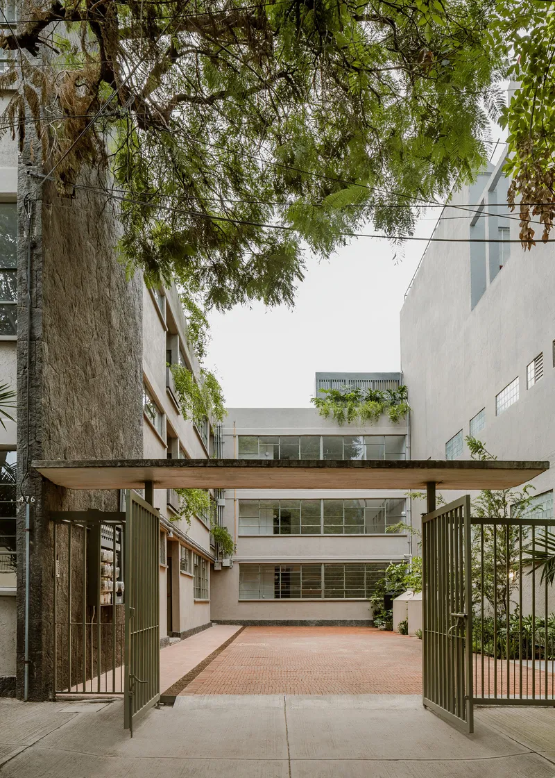 Street entrance with green metal gates under a concrete canopy framed by tree branches