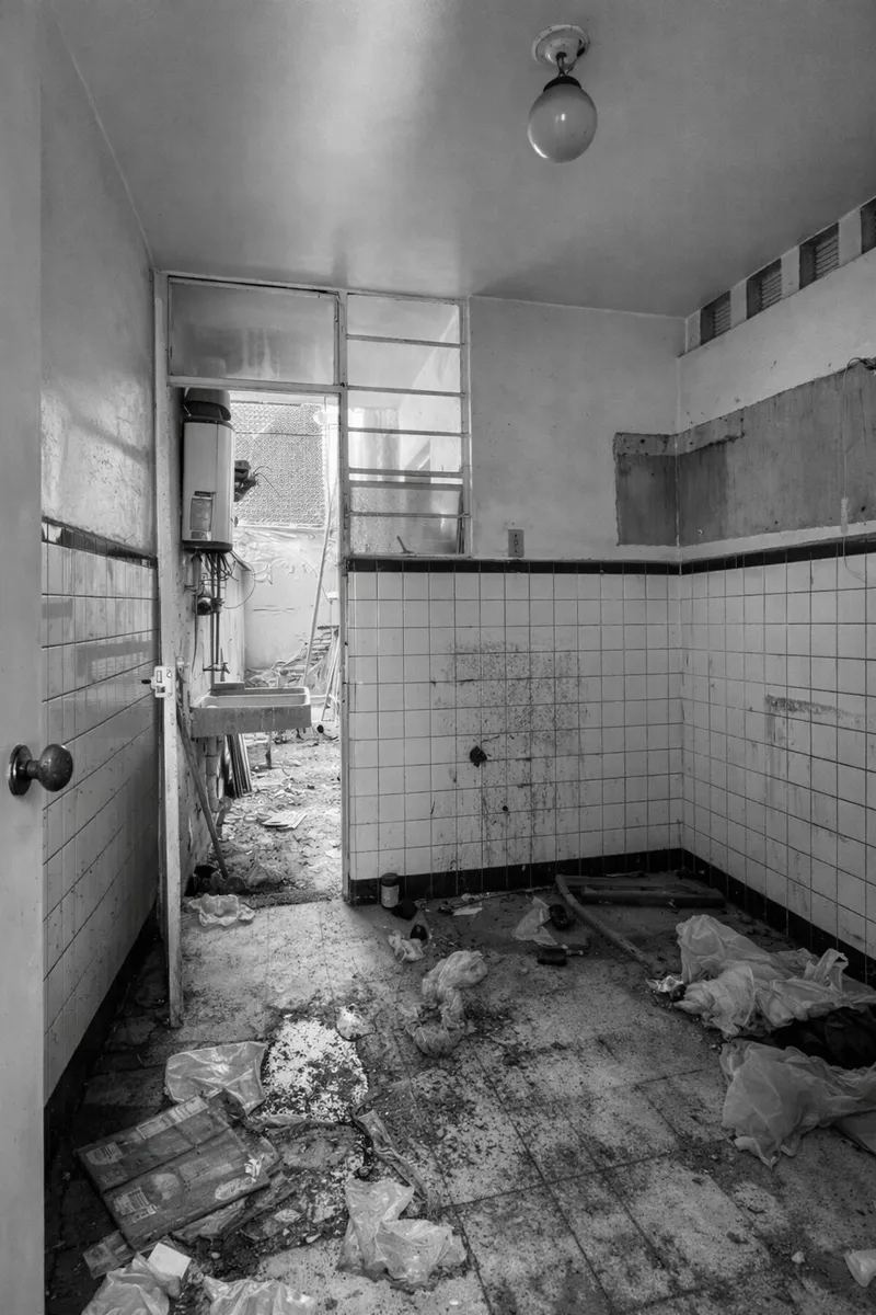 Abandoned bathroom with white tile wainscot and debris scattered across the floor