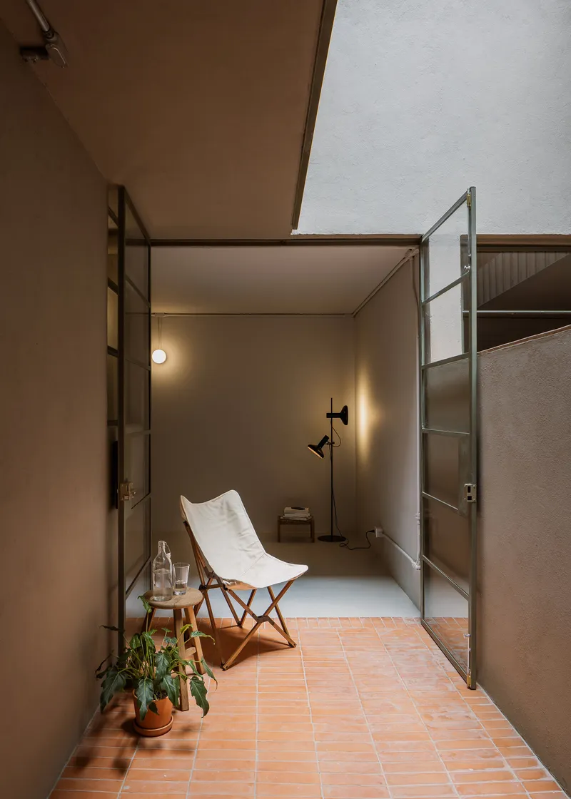Private terrace with terracotta tile flooring and glass door opening to an interior room at dusk