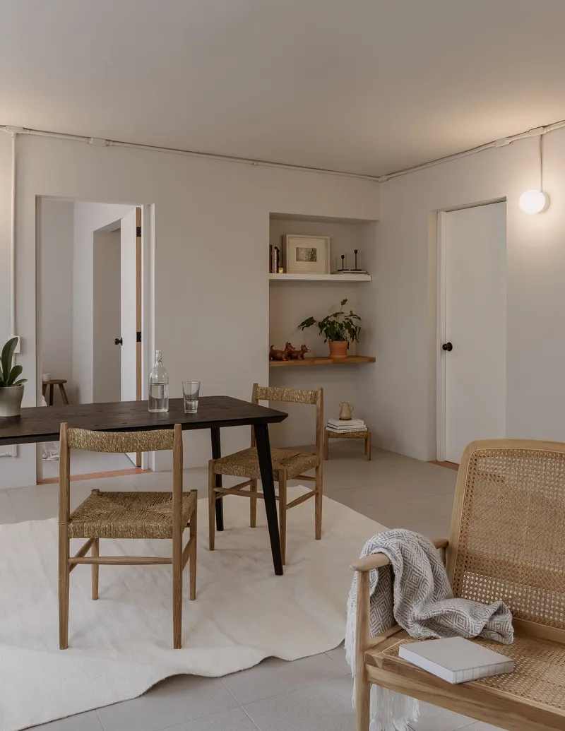 Dining area with woven rush chairs around a dark timber table and built-in shelving with potted plant