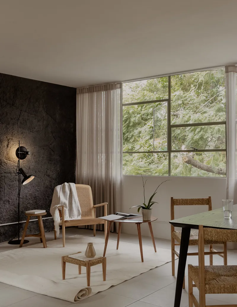 Living space with gridded steel window framing a tree canopy and textured dark feature wall