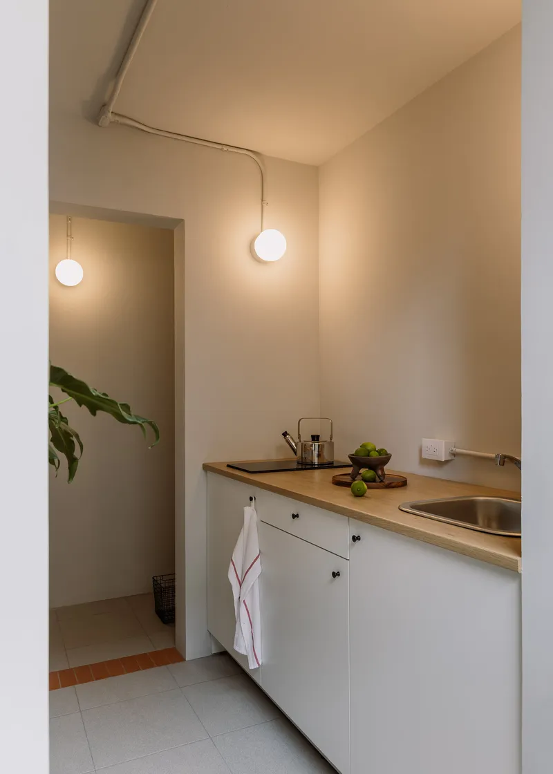 Compact kitchen with timber benchtop and white cabinetry beneath exposed conduit and globe pendant