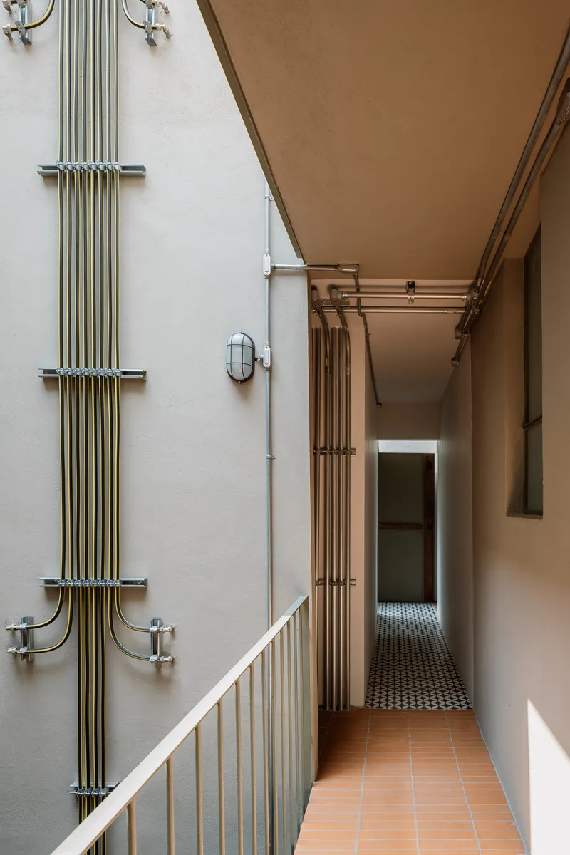 Corridor with exposed brass conduit running along the white wall and terra cotta tile floor