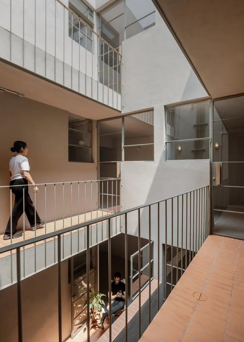 Interior courtyard with metal railings and a person walking on the upper level in daylight