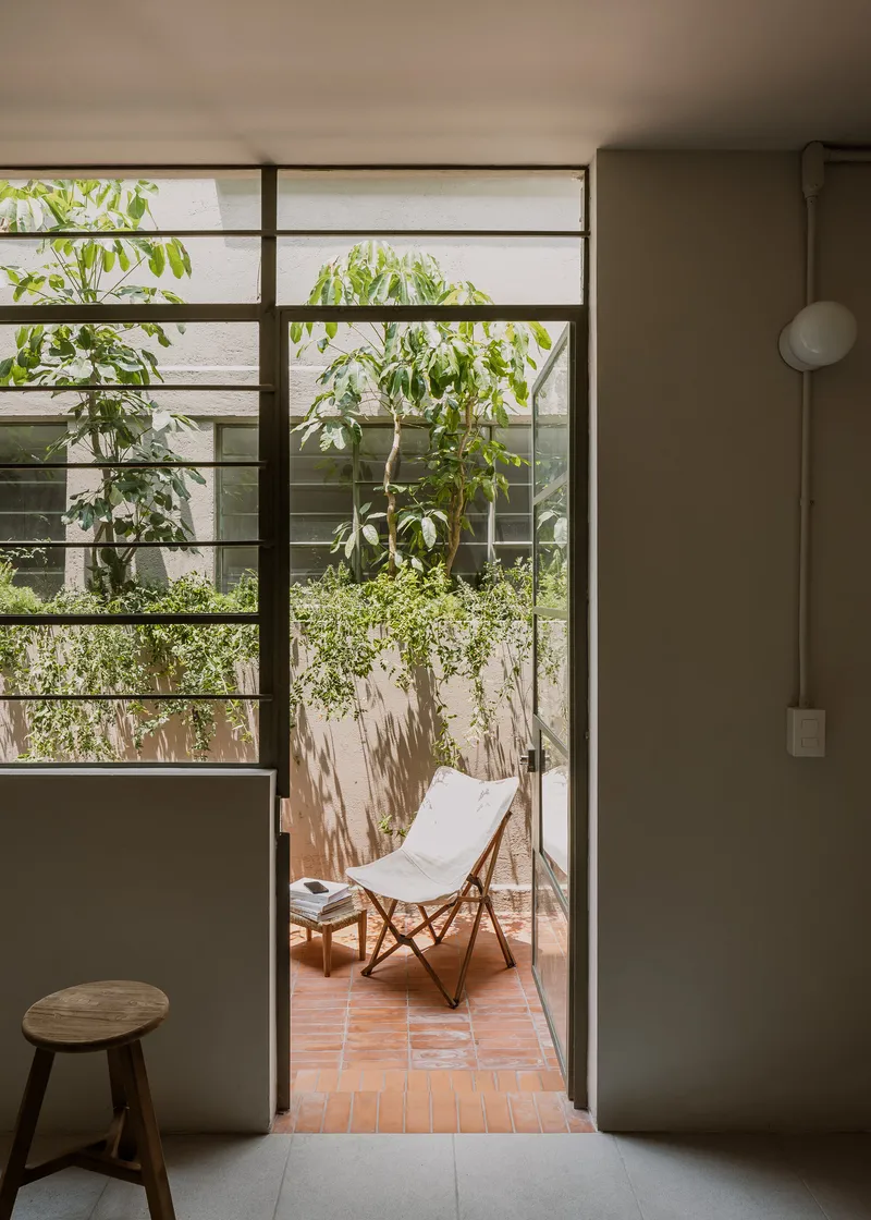 Glass door opening onto a terrace with a folding chair beneath green foliage