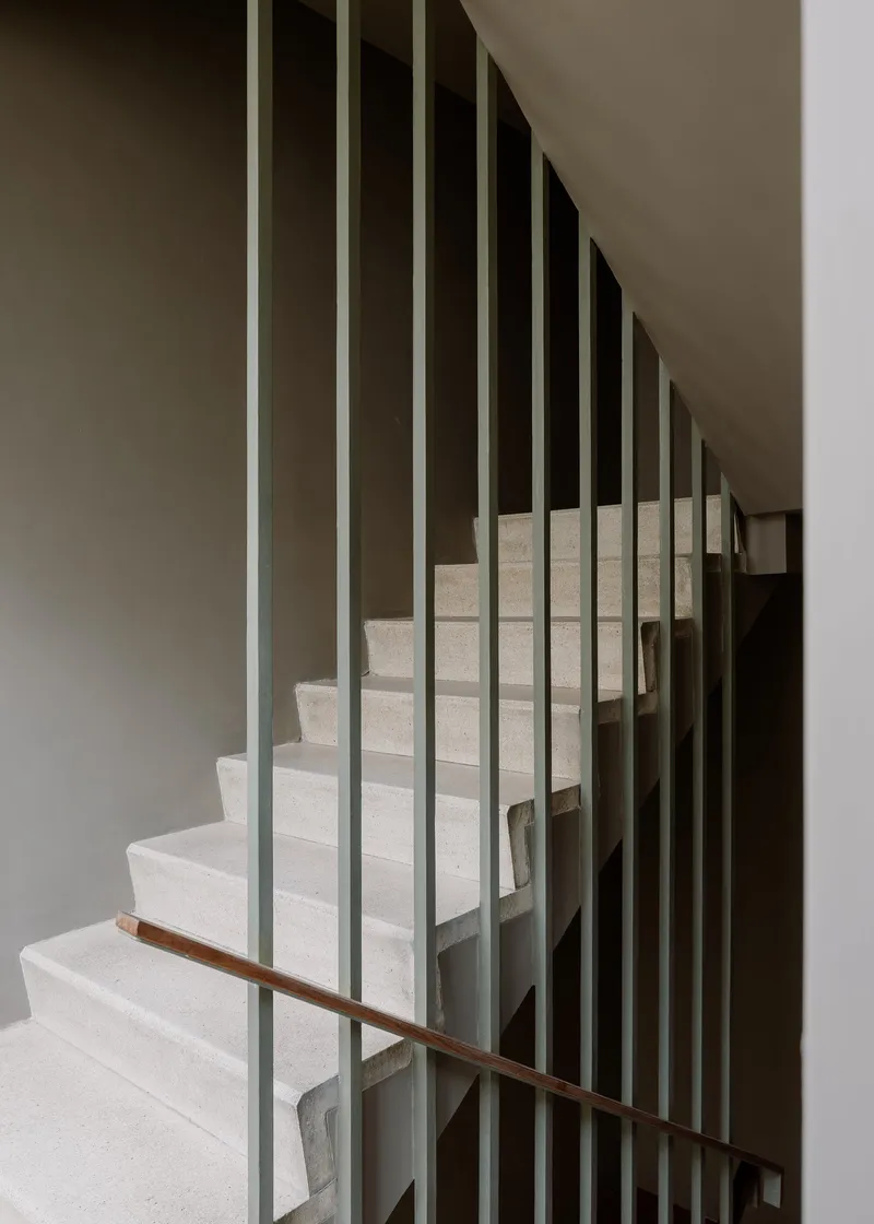 Staircase with vertical metal balusters and a timber handrail ascending between white walls