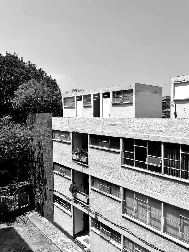 Concrete residential block with horizontal band windows and balconies beneath mature trees