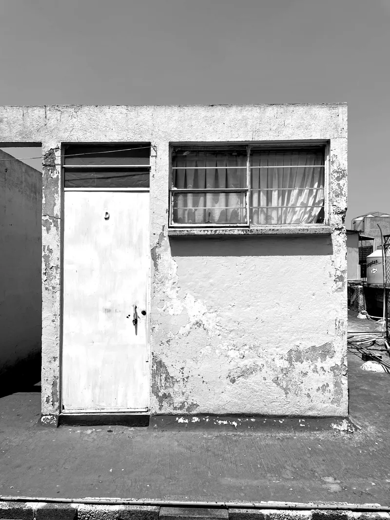 Weathered concrete facade with metal door and horizontal window under direct sunlight