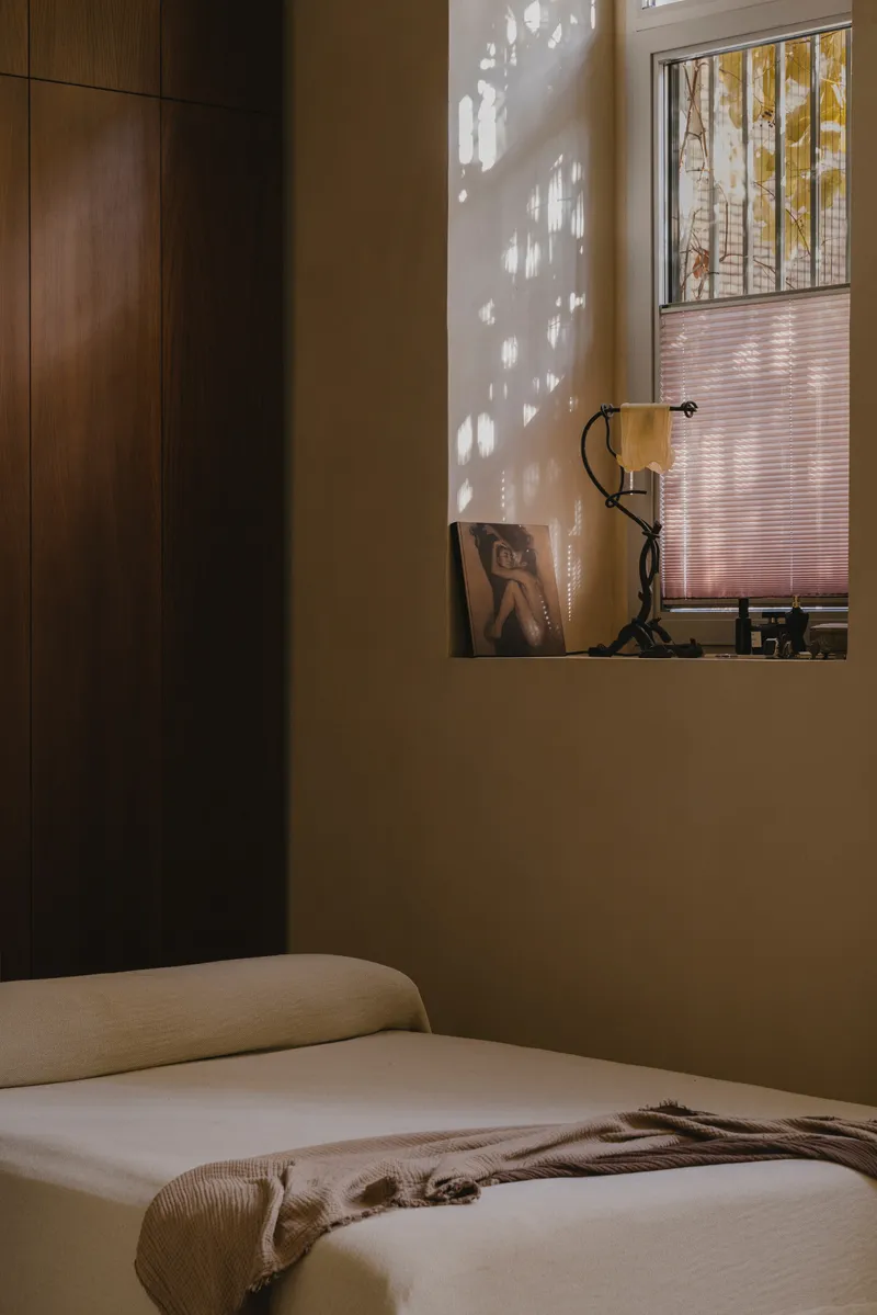 Bedroom view toward the recessed wall niche with dark timber cabinetry and filtered daylight casting shadows