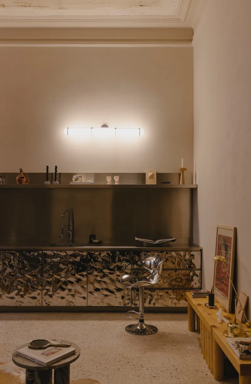 Living area with textured metallic cabinets beneath a terrazzo counter and original ceiling molding illuminated by a linear sconce