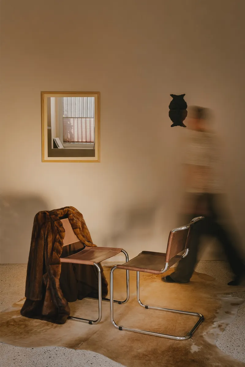 Timber-framed window niche and wall-mounted owl sculpture with figures moving past leather cantilever chairs