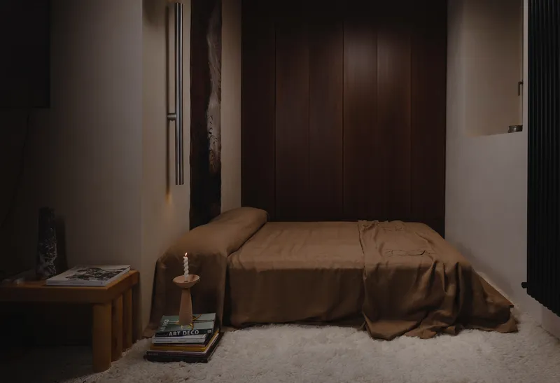 Bedroom nook with low bed facing vertical timber wardrobe panels in evening light