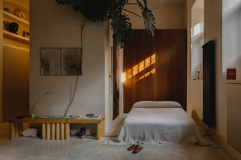 Sleeping alcove with timber wall panels casting striped light onto the white bedding at dusk