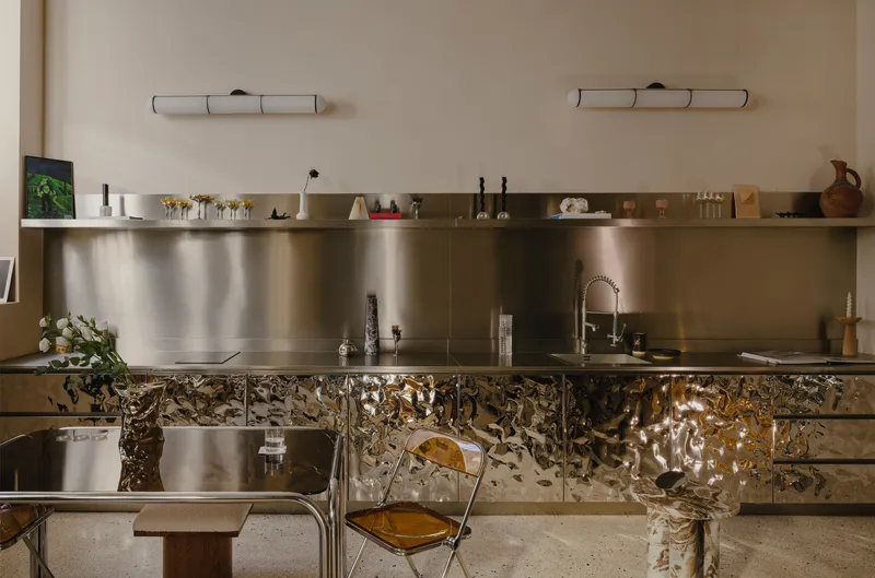 Kitchen with stainless steel backsplash and textured metallic cabinet fronts beneath a floating shelf