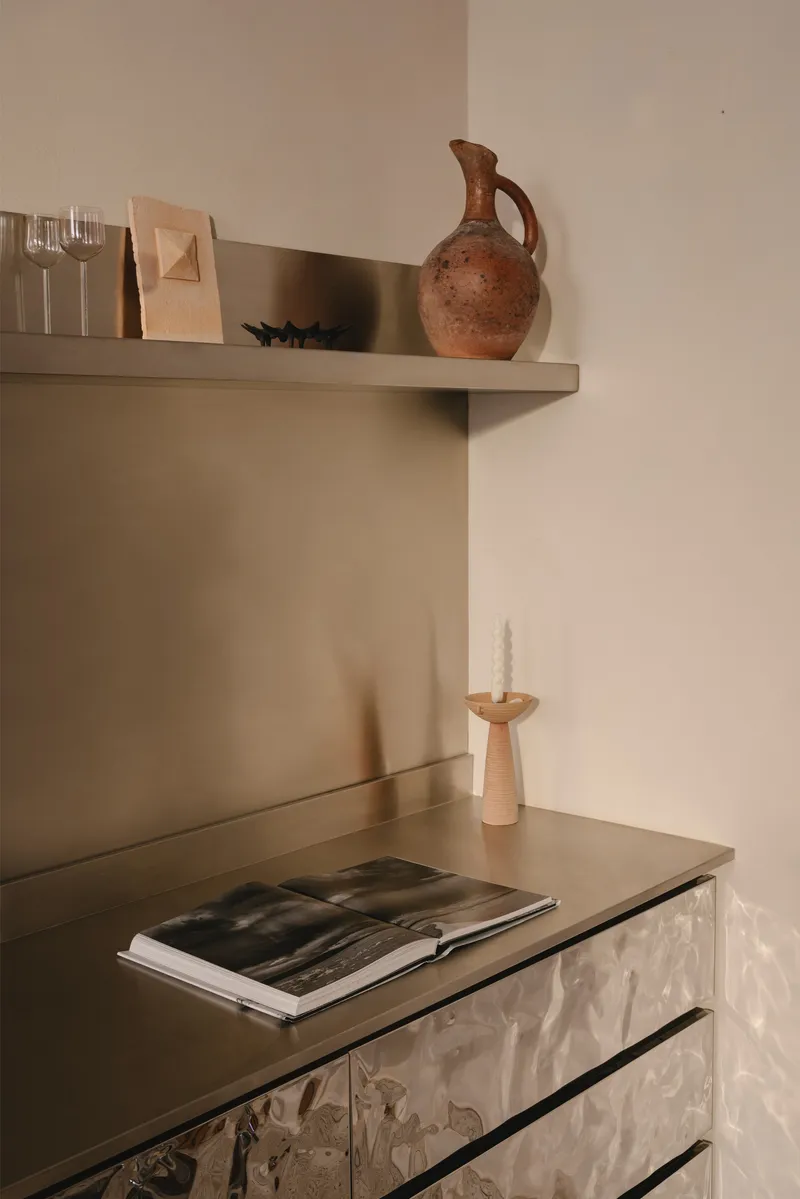 Detail of metallic cabinet with textured surface below a shelf holding a terracotta vessel
