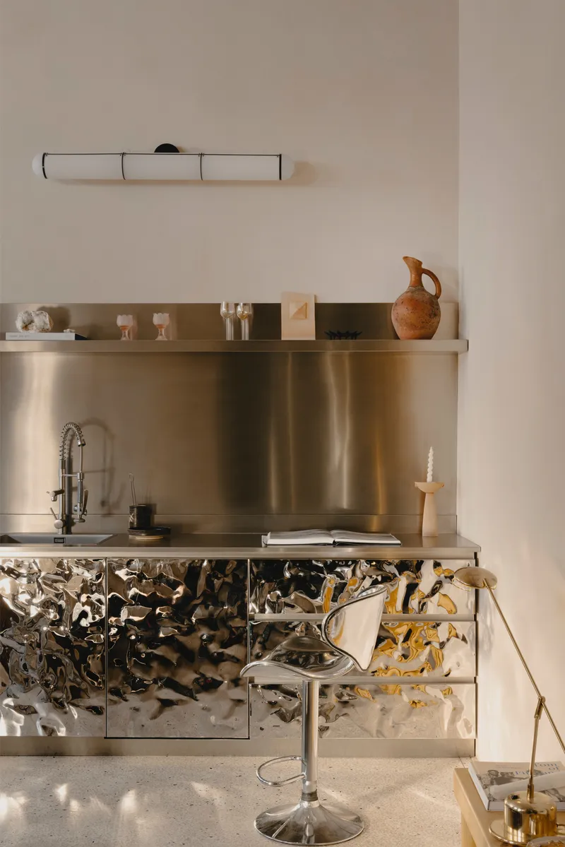 Kitchen niche with stainless steel backsplash above cabinets wrapped in reflective textured metal
