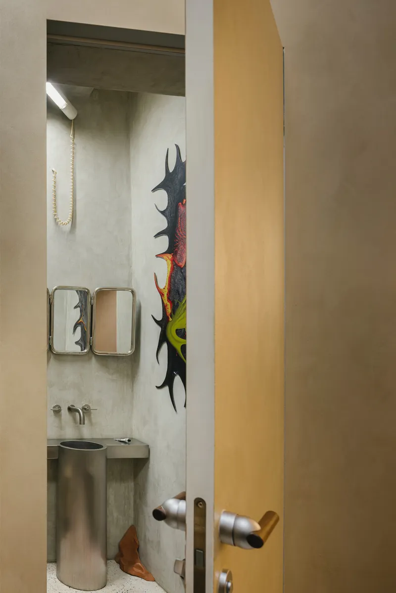 View through open timber door into bathroom with concrete sink and painted sculpture on wall