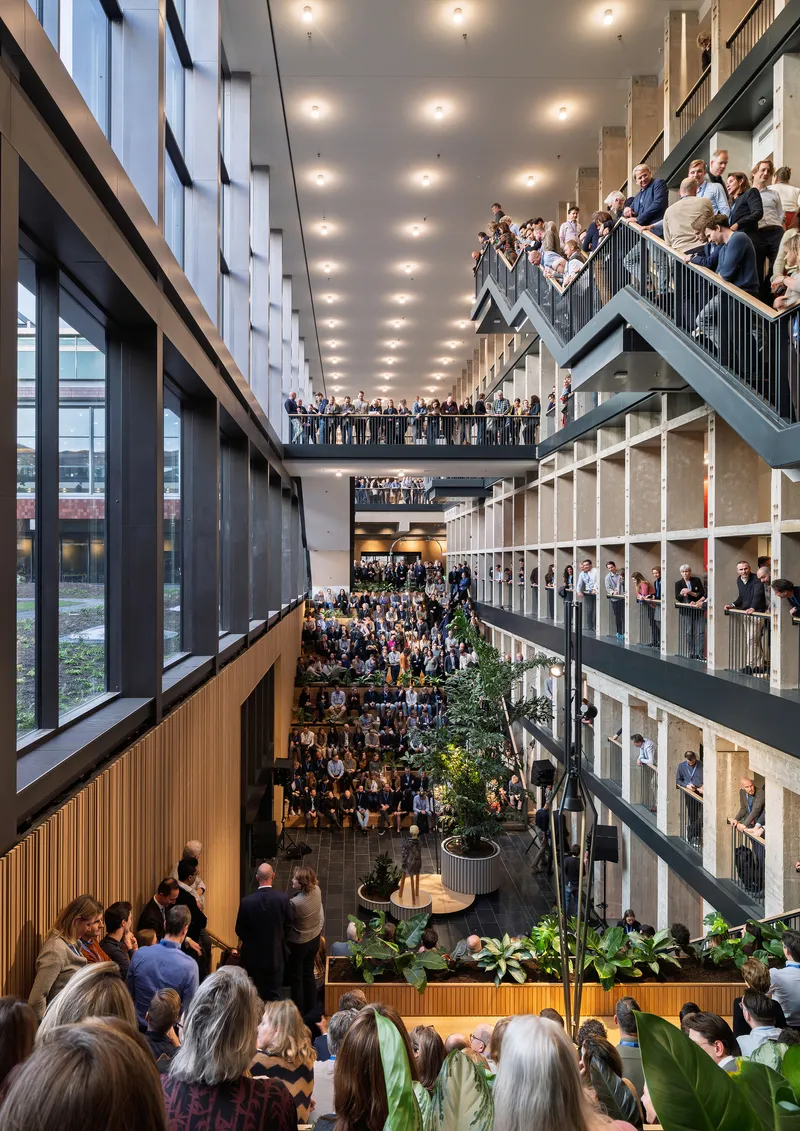 Multi-story atrium packed with people on balconies and stairs around planted greenery at ground level