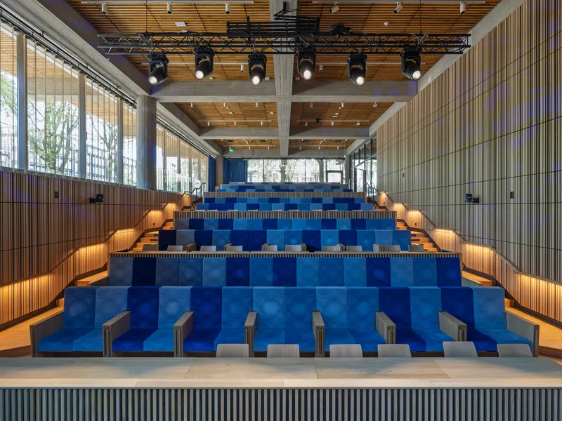 Auditorium with blue tiered seating, timber ceiling, theatrical lighting and vertical wall cladding