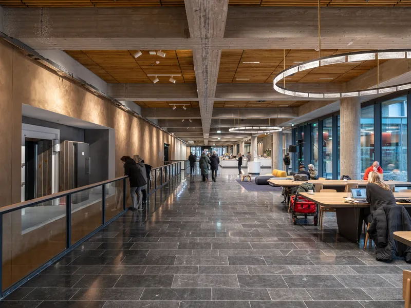 Circulation corridor with dark stone floor, timber ceiling panels, circular pendant lights and people gathering