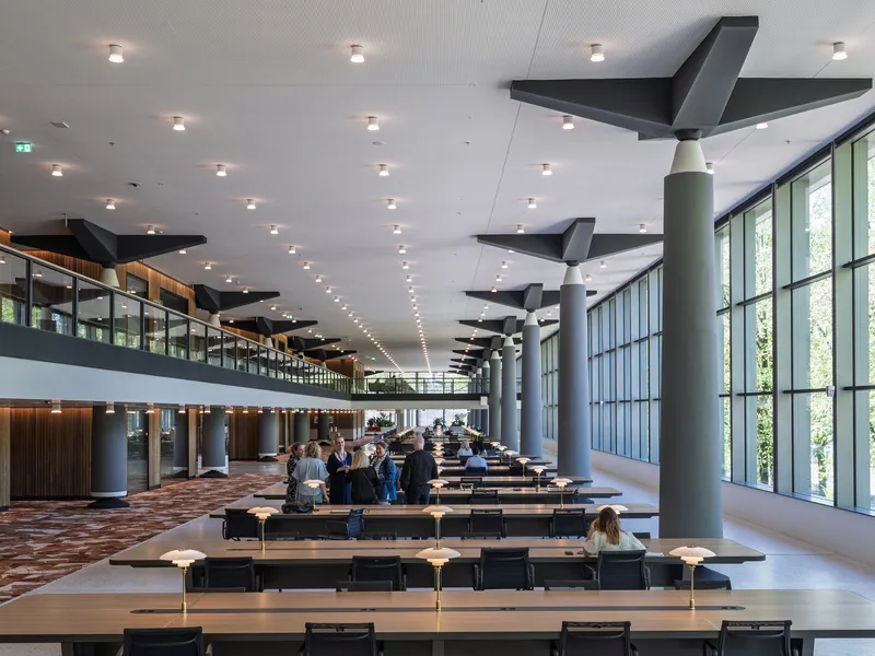 Double-height reading room with long study tables, cylindrical columns, and angular black ceiling baffles