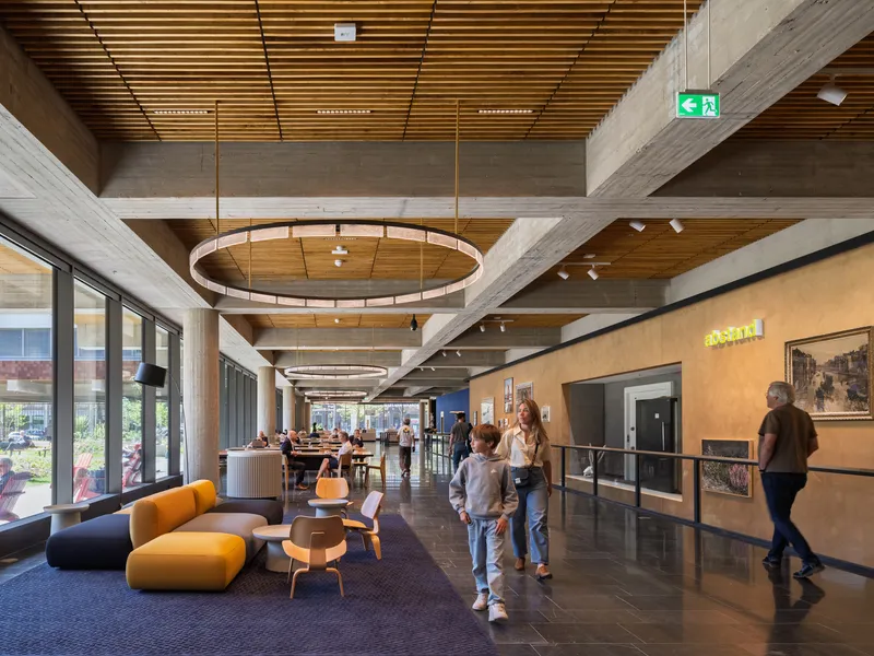 Corridor with timber ceiling and circular pendant lights as visitors walk past yellow display panels