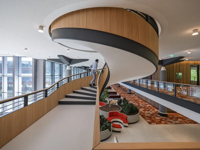 Spiral staircase with timber paneling and perforated ceiling wrapping around an atrium with planted floor