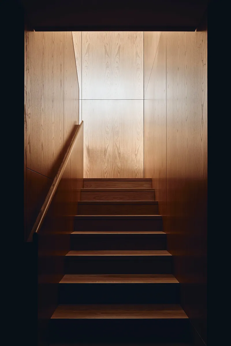 Timber staircase with cantilevered treads and blonde wood wall panels illuminated from above