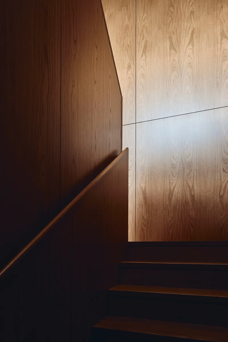 Detail of timber handrail and wall paneling junction at staircase with contrasting wood tones